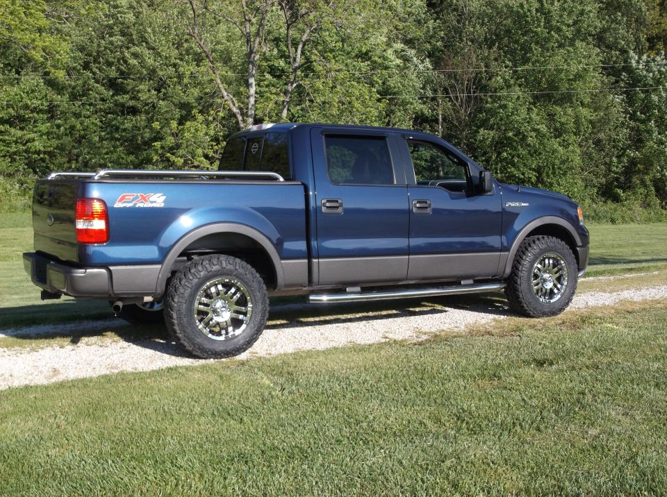 Blue Ford F-150 SuperCrew pickup truck with chrome wheels and side steps, viewed from the rear three-quarter angle