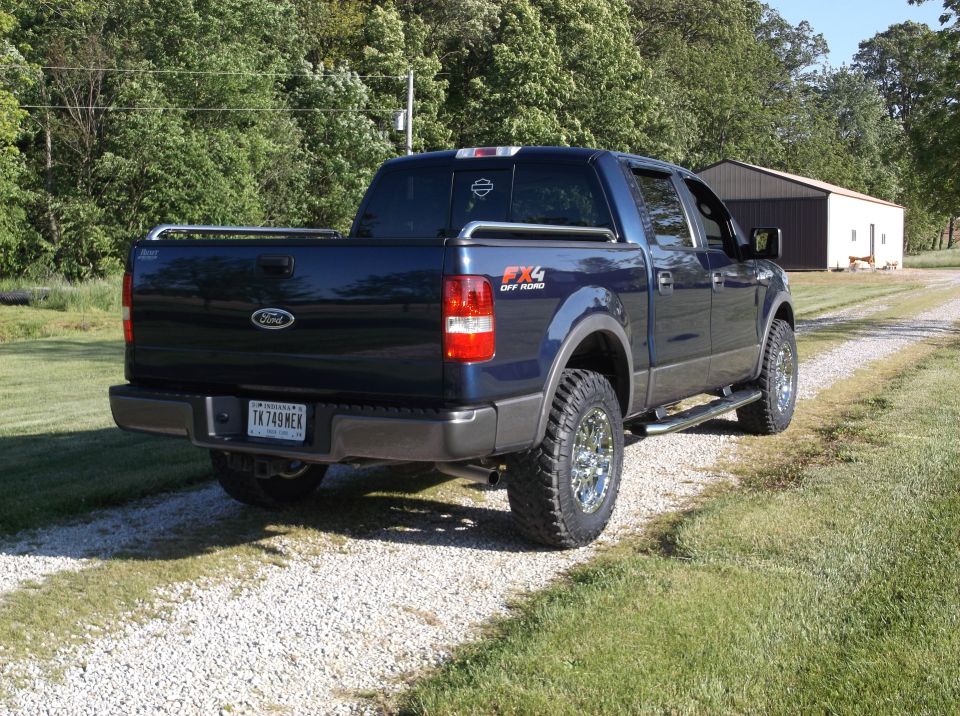 Dark blue Ford F-150 pickup truck with chrome wheels and FX4 Off Road decal, parked on a gravel driveway