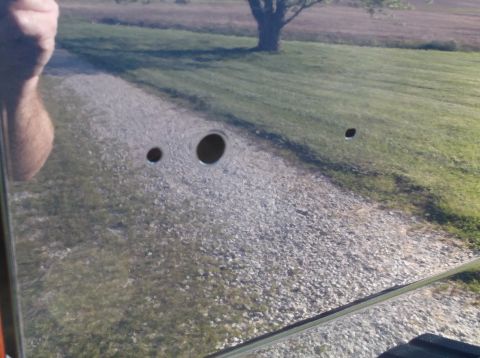 2005 Ford F-150 - A vehicle door shows three drilled holes, with a reflection of a rural landscape in its surface.