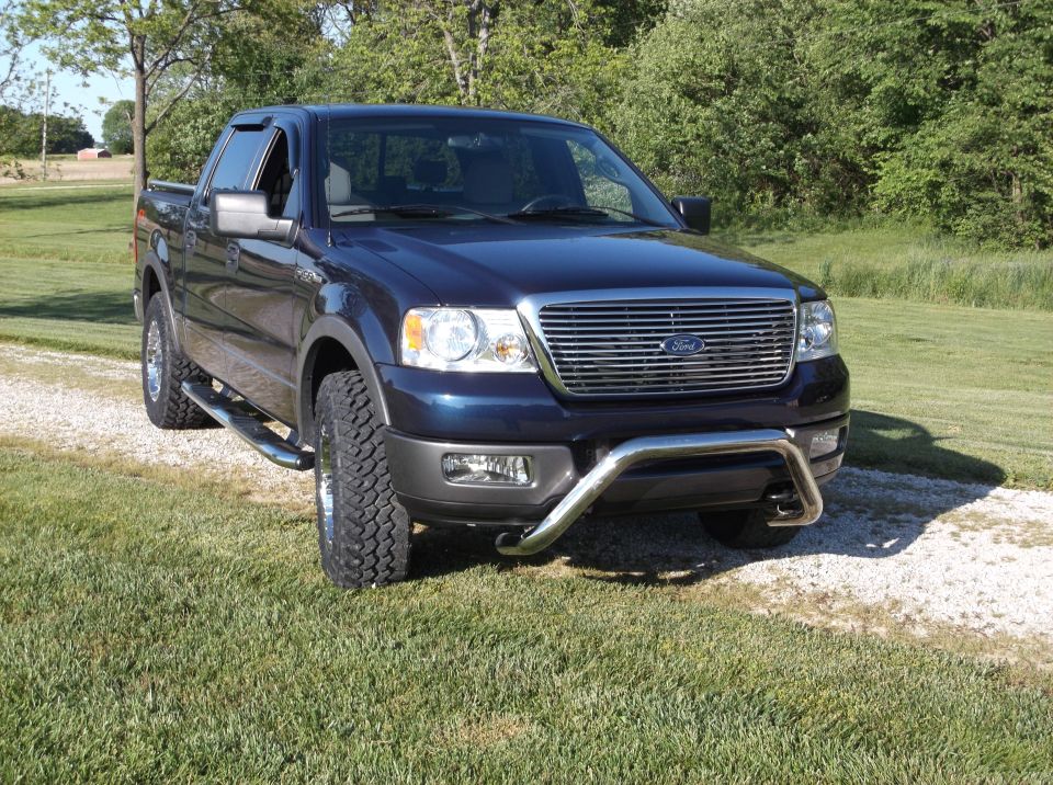 Dark blue Ford F-150 pickup truck with chrome grille guard parked on a gravel driveway