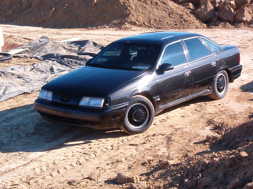 Black four-door sedan with ground effects and lace alloy wheels parked on dirt