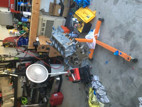1987 Ford Bronco - An engine block is mounted on an orange engine stand amidst various tools and equipment in a garage.