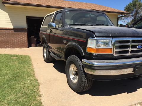 1994 Ford Bronco - A black Ford Bronco with a white top is parked in front of a garage.