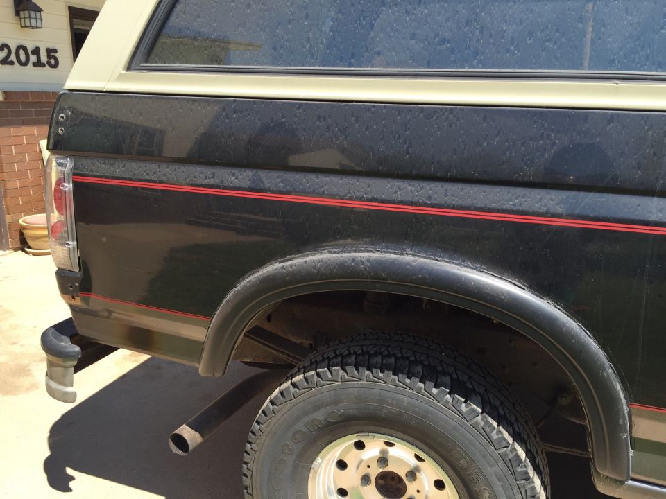 Rear quarter panel of a black Ford Bronco with red pinstripes. House number 2015 is visible on the building in the background