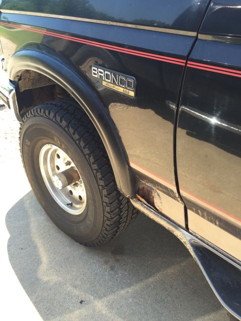 1994 Ford Bronco - Close-up of the side of a black Ford Bronco, highlighting its 'Eddie Bauer' trim and some rust damage.