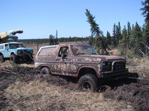 1985 Ford Bronco - Two SUVs are stuck in the mud, with one being towed out by another vehicle.