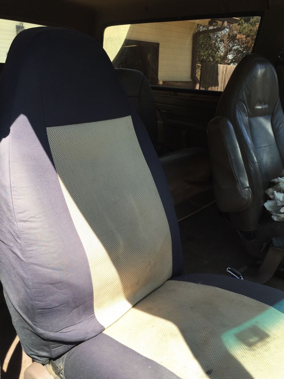 Interior view of a vehicle showing a fabric seat cover over the driver's seat and a leather passenger seat