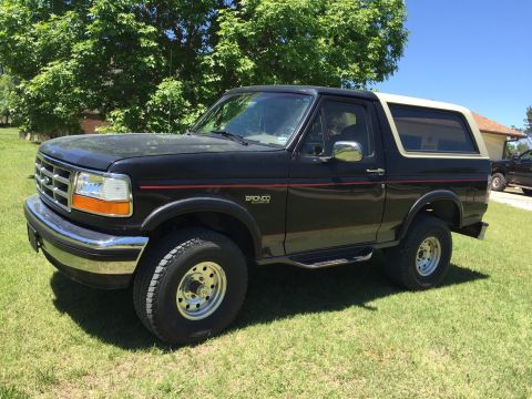 1994 Ford Bronco - This black Ford Bronco with a tan top is parked on a grassy lawn.