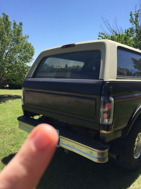 1994 Ford Bronco - The rear of a black and tan Ford Bronco is visible, parked on a grassy lawn under a clear blue sky.