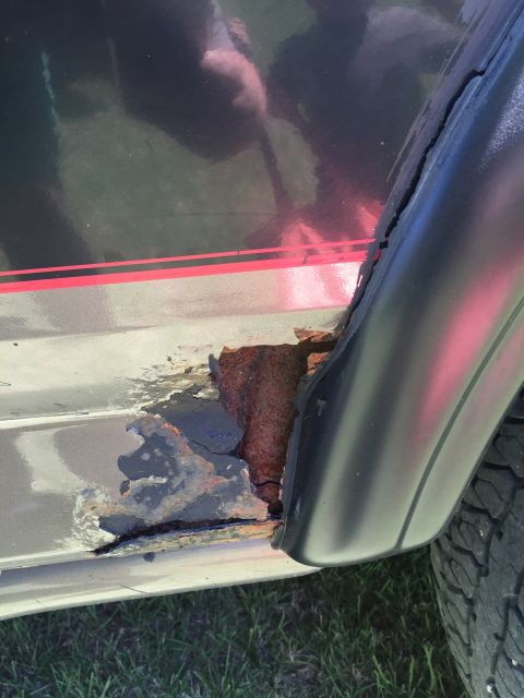 1994 Ford Bronco - Significant rust has eaten away at the vehicle's lower body panel, revealing extensive corrosion.