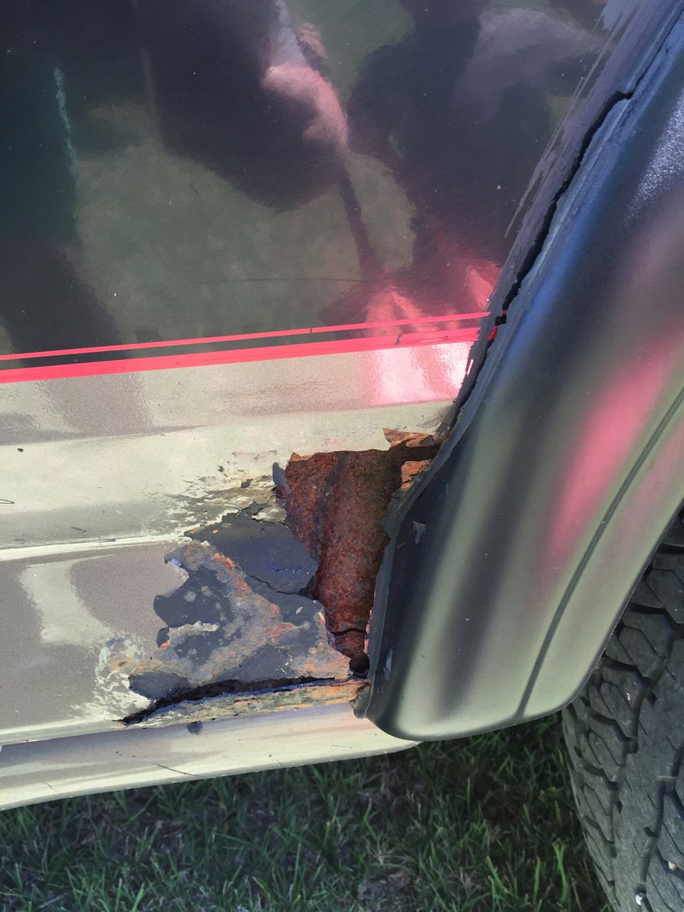 Close-up of severe rust damage on the lower body panel of a vehicle, near the rear wheel well