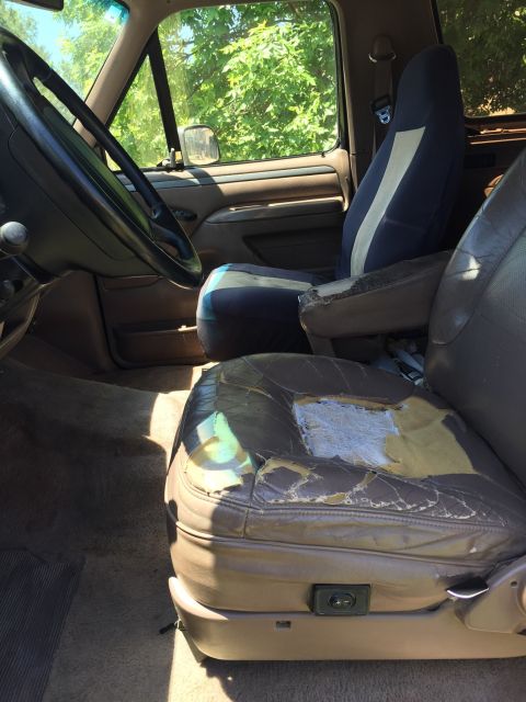 1994 Ford Bronco - The interior of a 1992 Ford Bronco shows significant wear on the driver's seat and a blue cloth passenger seat.