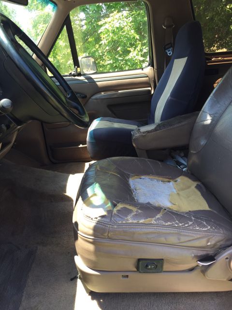 1994 Ford Bronco - The interior of this 1994 Ford Bronco features worn leather seats and blue seat covers, offering a glimpse into its past use.