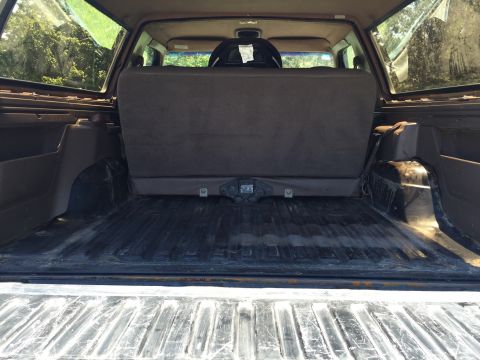 1994 Ford Bronco - The interior cargo area of an SUV shows folded rear seats and a tow hitch, with trees visible through the windows.