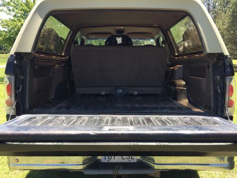 1994 Ford Bronco - The open tailgate reveals the cargo area of an SUV, with a folded rear seat visible inside.
