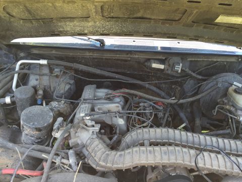1994 Ford Bronco - The engine bay of a vehicle is shown with various mechanical parts and wiring.