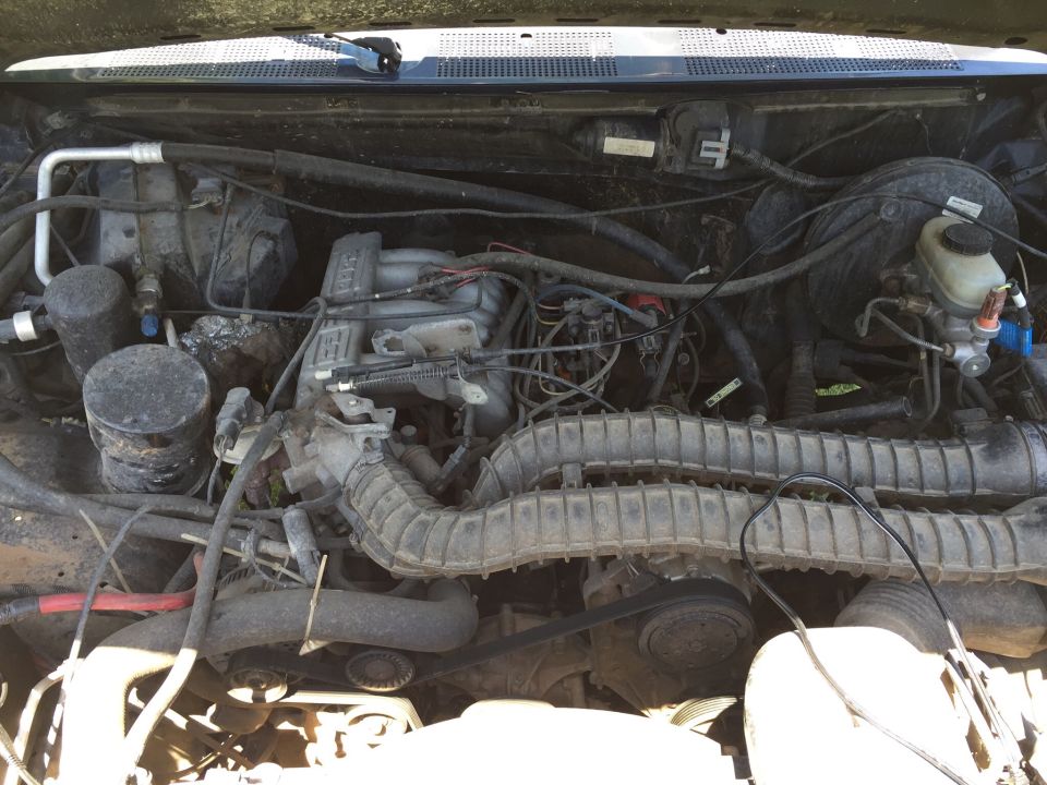 Engine bay of a 1994 Ford Bronco. Visible components include the air intake, engine block, and brake fluid reservoir