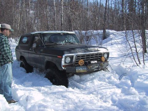 1985 Ford Bronco - Ford Bronco stuck in snow with a person standing nearby. The vehicle has a winch and decorative smiley face lights on the bumper.