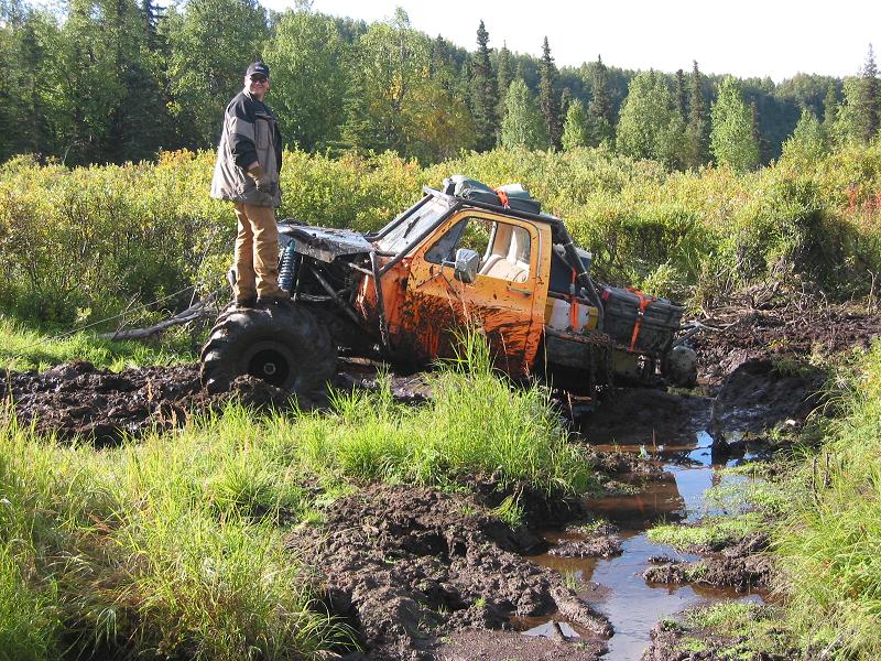 Orange tube-frame off-road rig stuck in deep mud, man standing on front tire
