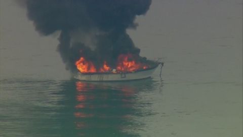 1991 Ford Bronco - A boat is seen on fire in the water, with thick black smoke billowing into the sky.