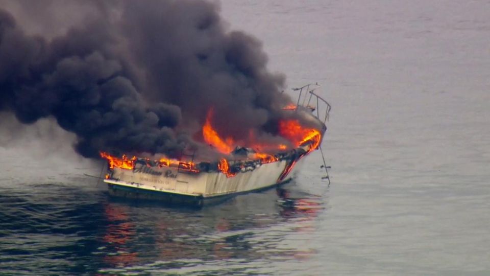 White boat engulfed in flames and black smoke on the water
