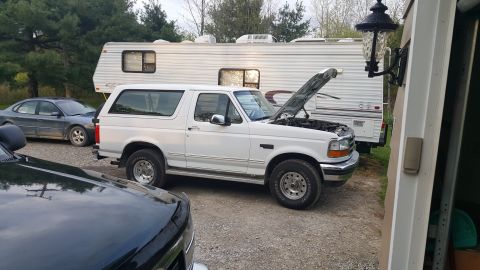 1995 Ford Bronco - A white Ford Bronco is parked outside with its hood up, next to a recreational vehicle.