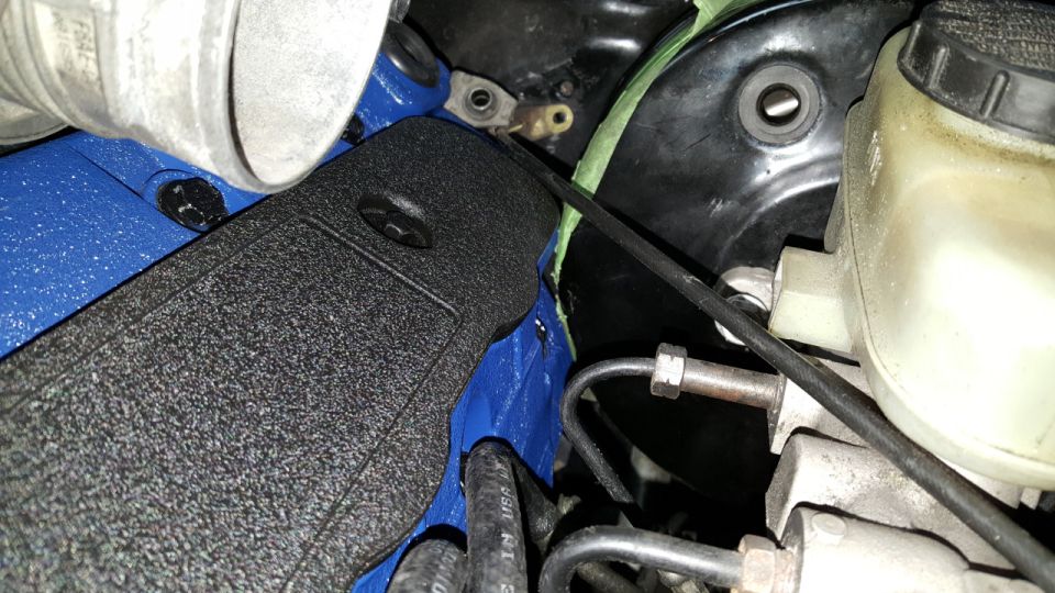 Engine bay with blue painted component, black textured cover, and brake fluid reservoir