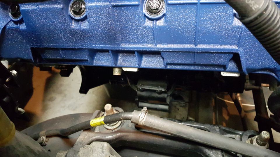 Close-up of a blue painted engine component with bolts and hoses visible