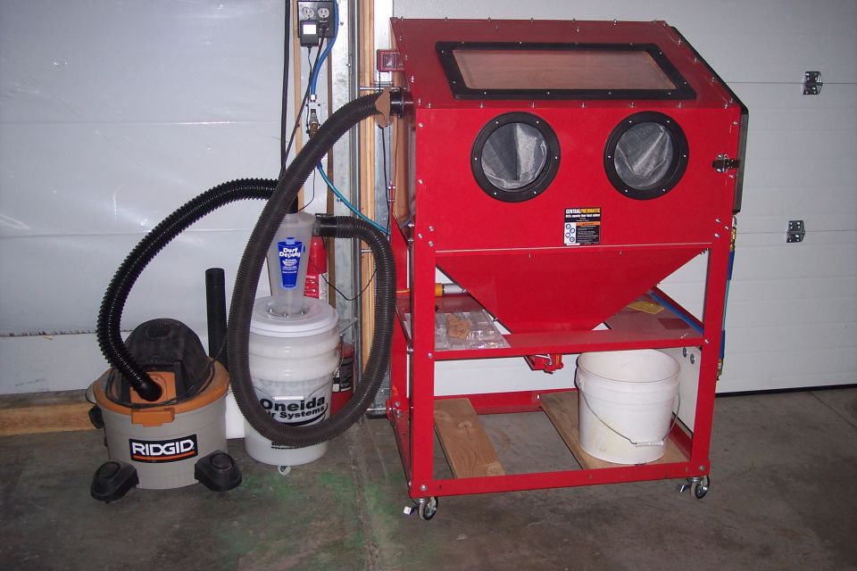 Red sandblaster cabinet with two glove ports, connected to a Ridgid shop vac and a dust collection system