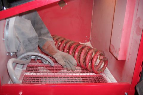1990 Ford Bronco - A coil spring is being cleaned inside a red sandblaster cabinet.