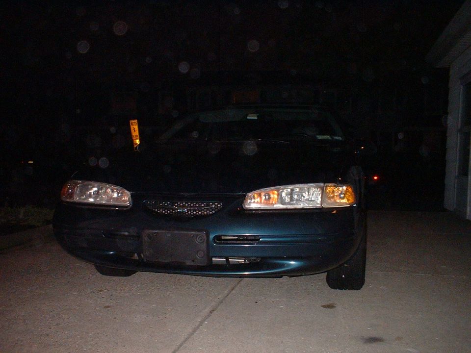 Dark green Ford Thunderbird coupe front view at night on a driveway, headlights lit by camera flash