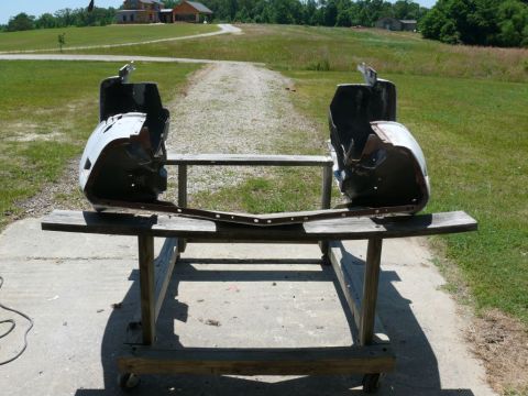 Two disassembled car fender sections and a bumper support bar on a wooden stand