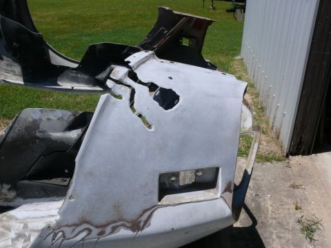 Damaged gray car bumper with large cracks and rust spots, showing a license plate mount