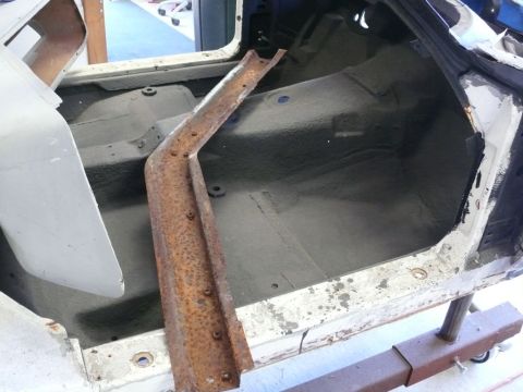 Car interior with rusted metal brace on floor, white body panel visible