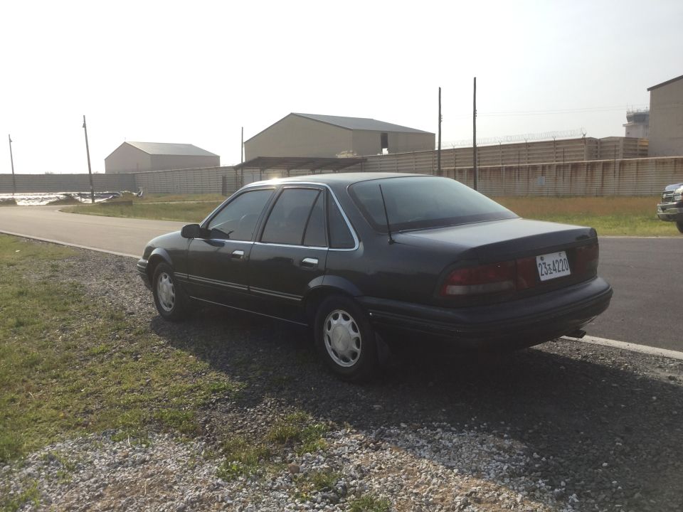 Dark sedan parked on gravel, rear view. License plate 2364220