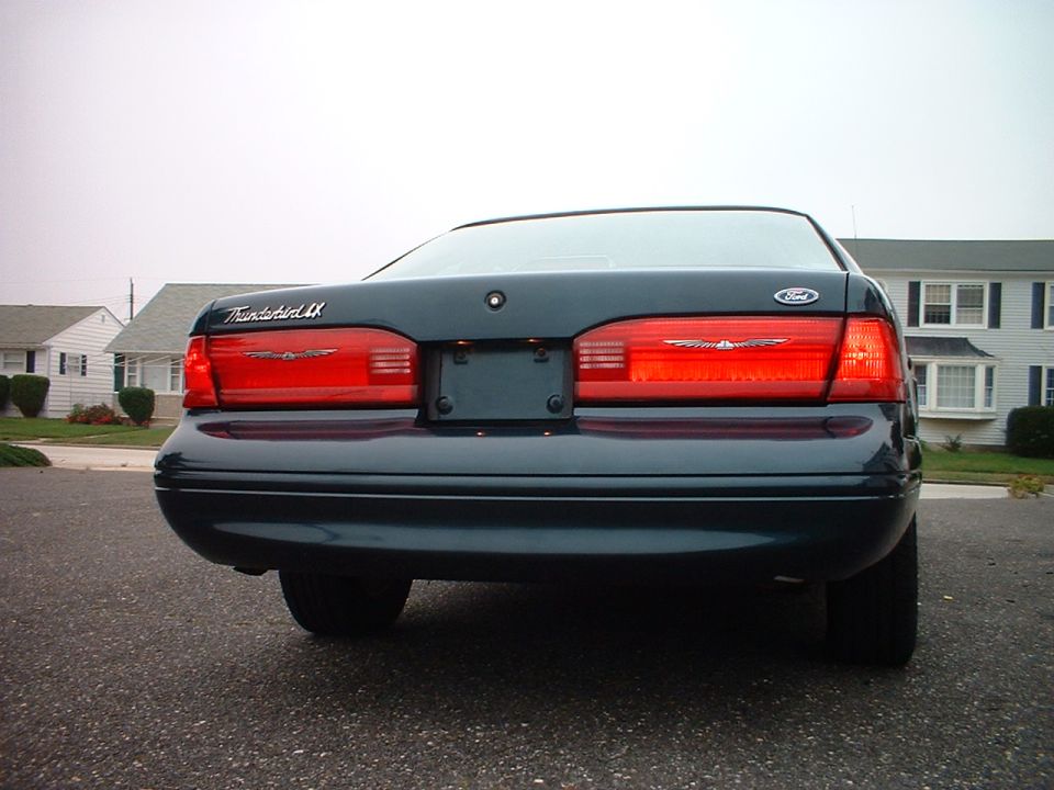 Rear view of dark green Ford Thunderbird LX coupe with full-width red taillights on residential street