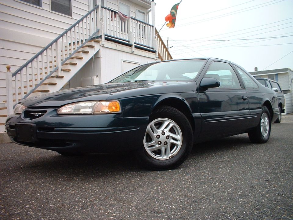 Dark green Ford Thunderbird coupe parked on pavement by a wooden staircase