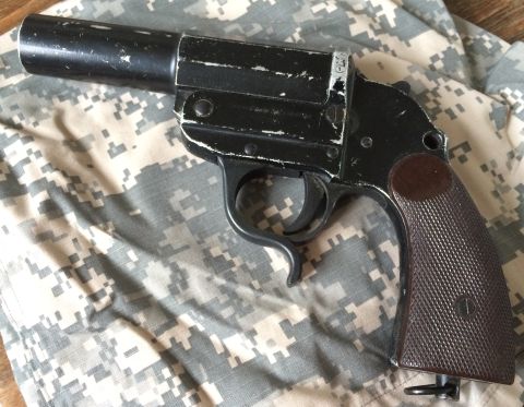 1987 Ford Bronco - A black flare gun with a textured grip is shown from a side angle on a camouflage background.