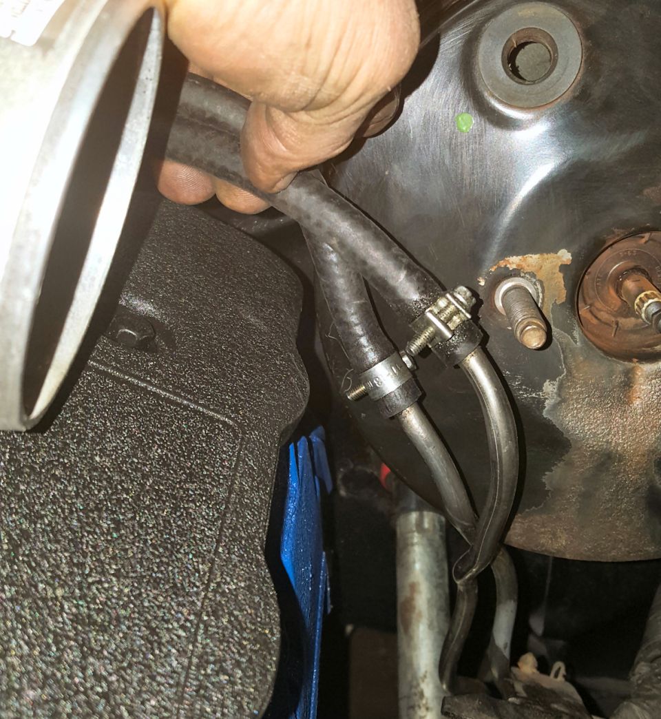 Hand holding two vacuum hoses connected to metal lines near engine components