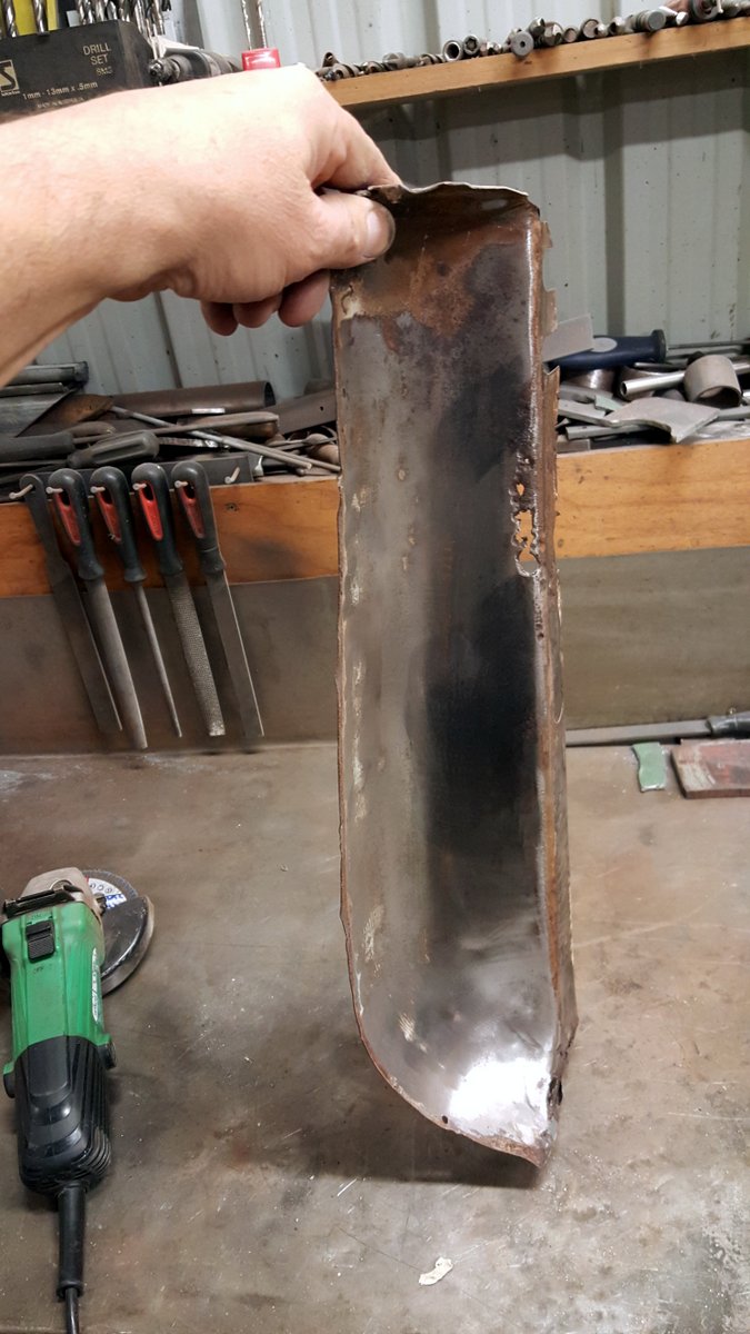 Rusted metal panel held by a hand over a workbench with tools
