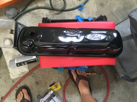 1987 Ford Bronco - A freshly painted black Ford valve cover sits on a red support, ready for installation.