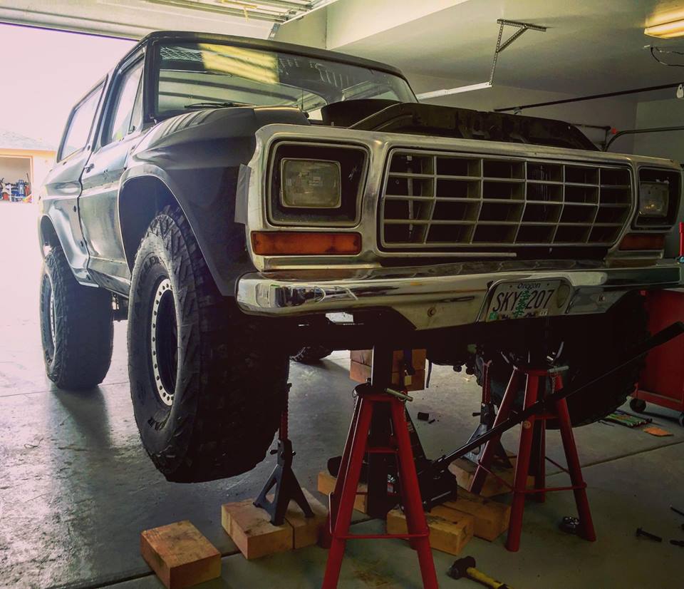 Front view of a 1979 Ford Bronco lifted on jack stands in a garage, hood up