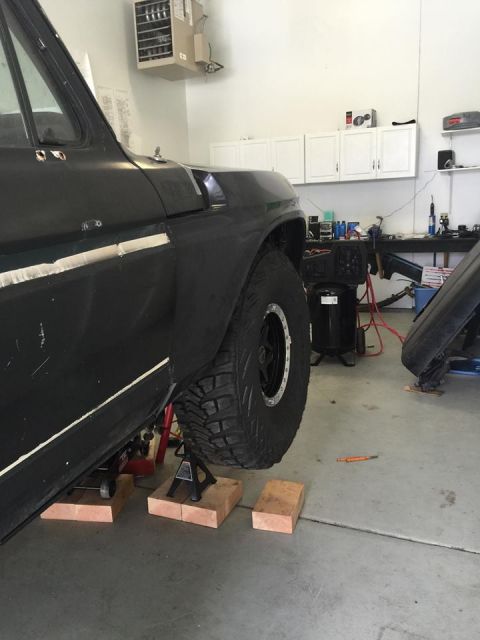 1979 Ford Bronco - A black SUV's fender and tire are elevated on jack stands in a garage, revealing its side profile and suspension.