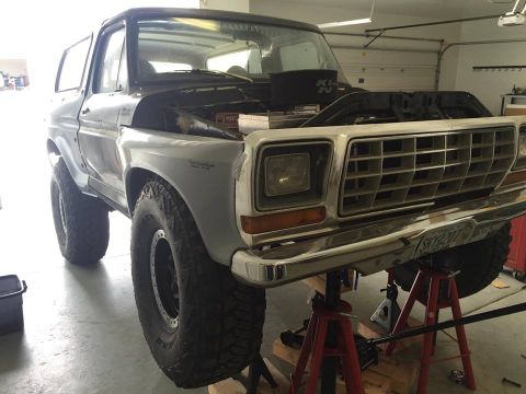 1979 Ford Bronco - A 1979 Ford Bronco is shown with its front end elevated on jack stands, undergoing maintenance with the hood open.