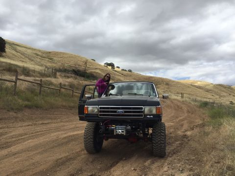 1989 Ford Bronco - A lifted black Ford truck with a winch is parked on a dirt road with a woman in the driver's seat.
