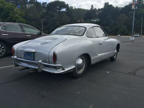 1968 Ford Mustang - Silver Volkswagen Karmann Ghia coupe seen from the rear, parked in a lot with another car.