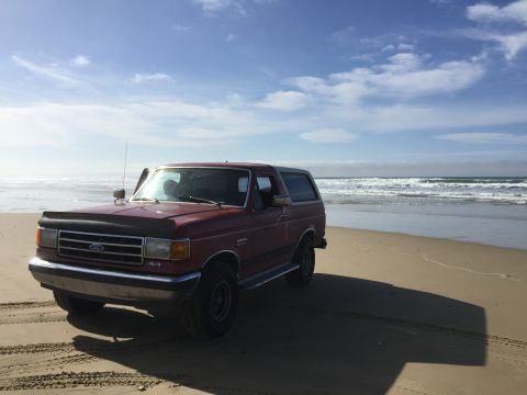 1991 Ford Bronco - This 1991 Ford Bronco is parked on the sand near the ocean waves.