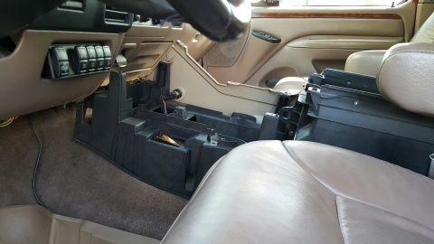 1996 Ford Bronco - Interior shot looking across a tan leather cab at the black center console base sitting in place with its lid and trim removed, exposing th…