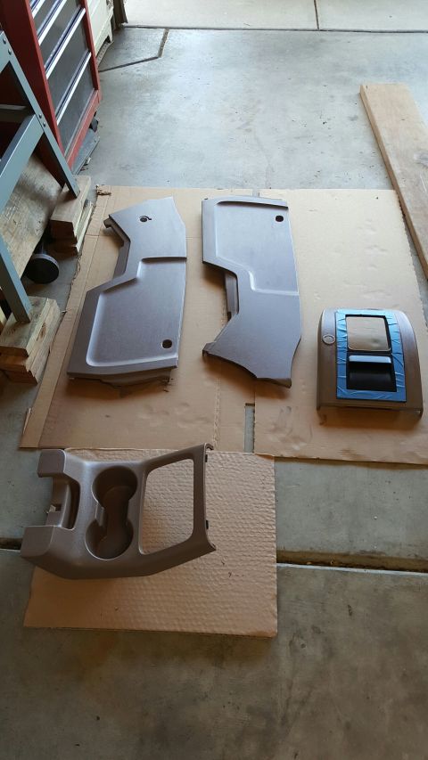 1996 Ford Bronco - Disassembled car interior parts, including a center console and trim pieces, are laid out on cardboard.
