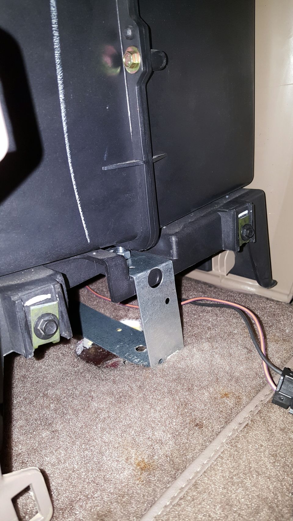 Black seat base on a custom steel mounting bracket with yellow zinc bolts over tan carpet